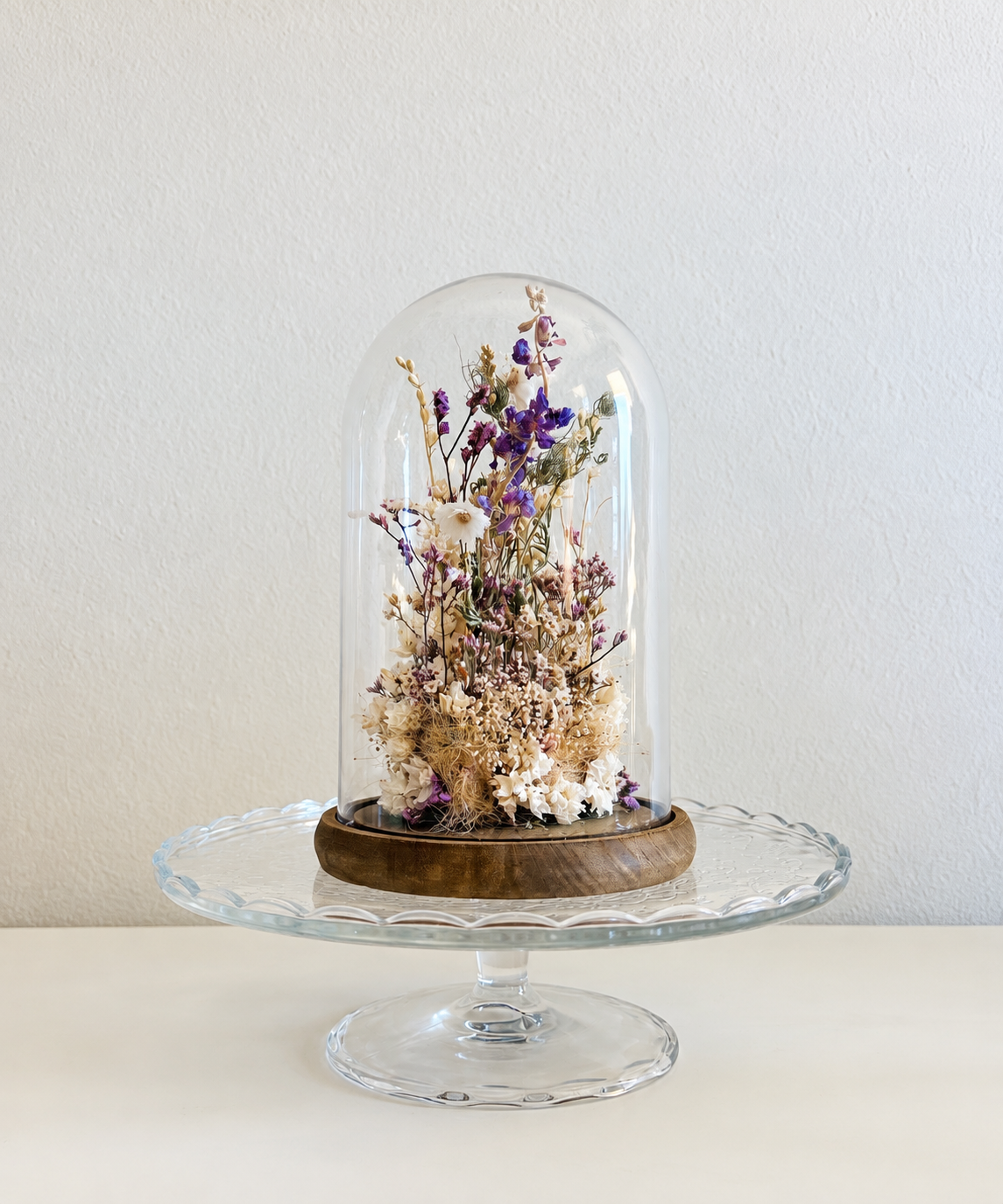 Hand-arranged dried flowers under a glass cloche on a wooden base